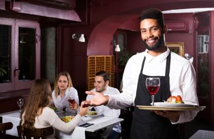 A waiter serving food and drinks to patrons  in a restaurant.