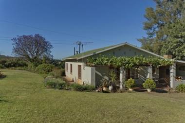 A picture of a self catering chalet building with grass all around and a porch with plants draped on the pillars.
